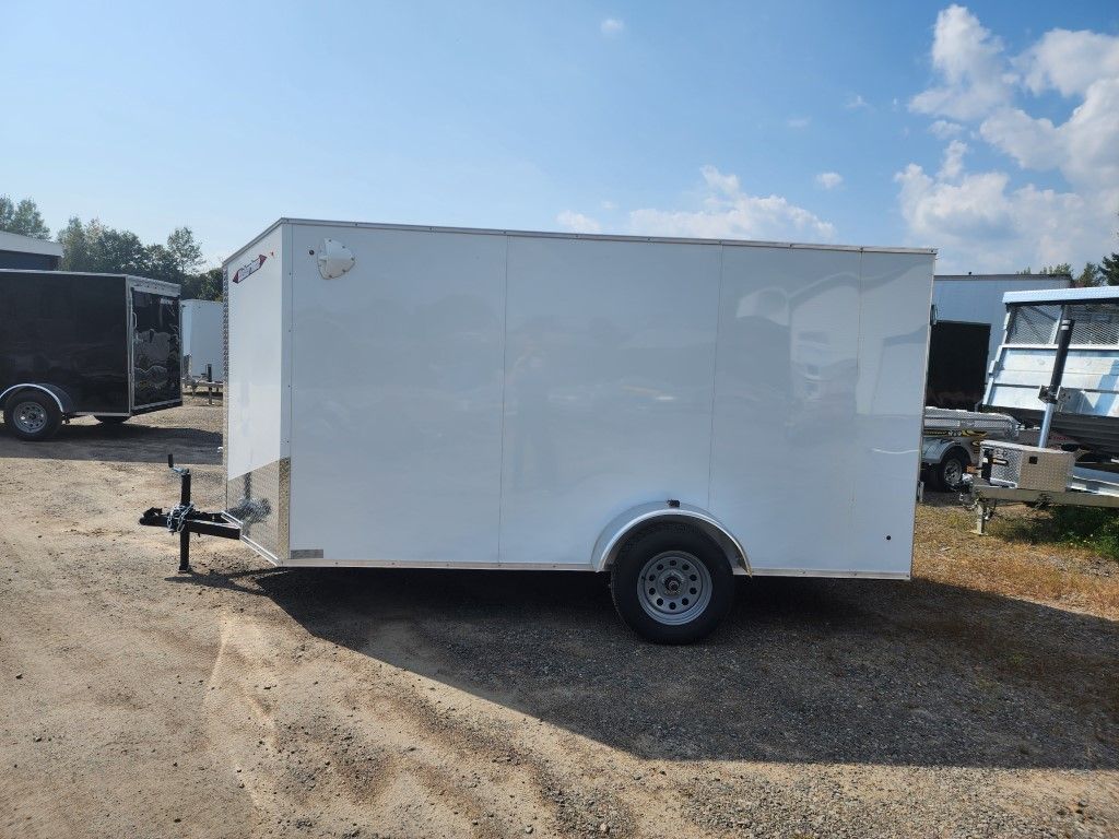 Remorque cargo blanche fermée sur un terrain gravillonné sous un ciel bleu.