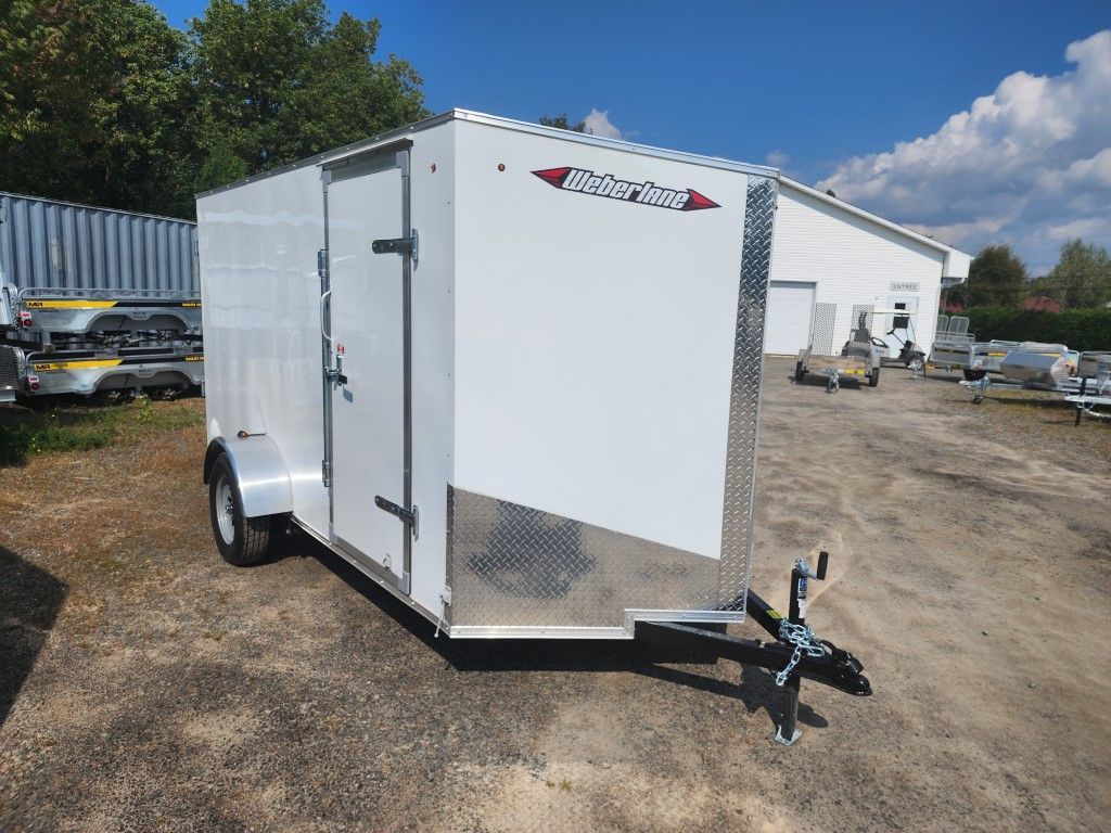 Remorque blanche fermée avec attelage noir, garée à l'extérieur.