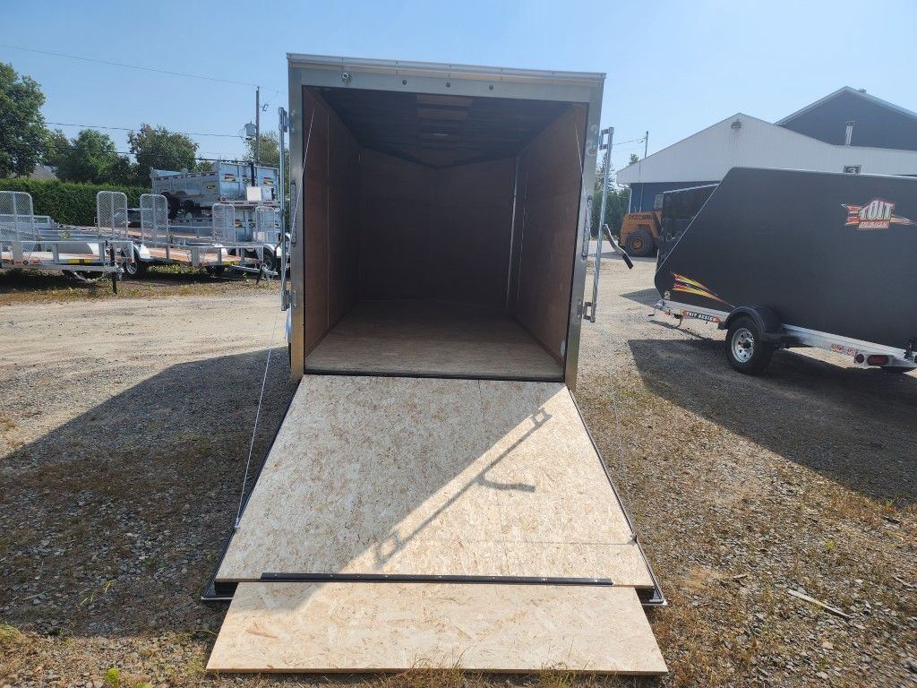 Remorque cargo ouverte avec rampe en bois déployée, à l'extérieur sur du gravier.