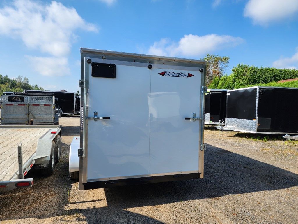 Remorque cargo blanche, portes fermées, sur un terrain gravillonné sous un ciel bleu.