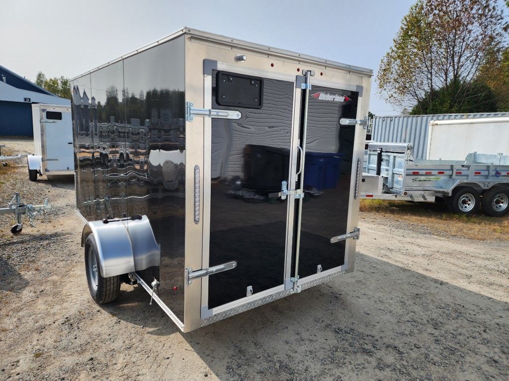 Remorque cargo fermée noire avec garniture argentée sur gravier.