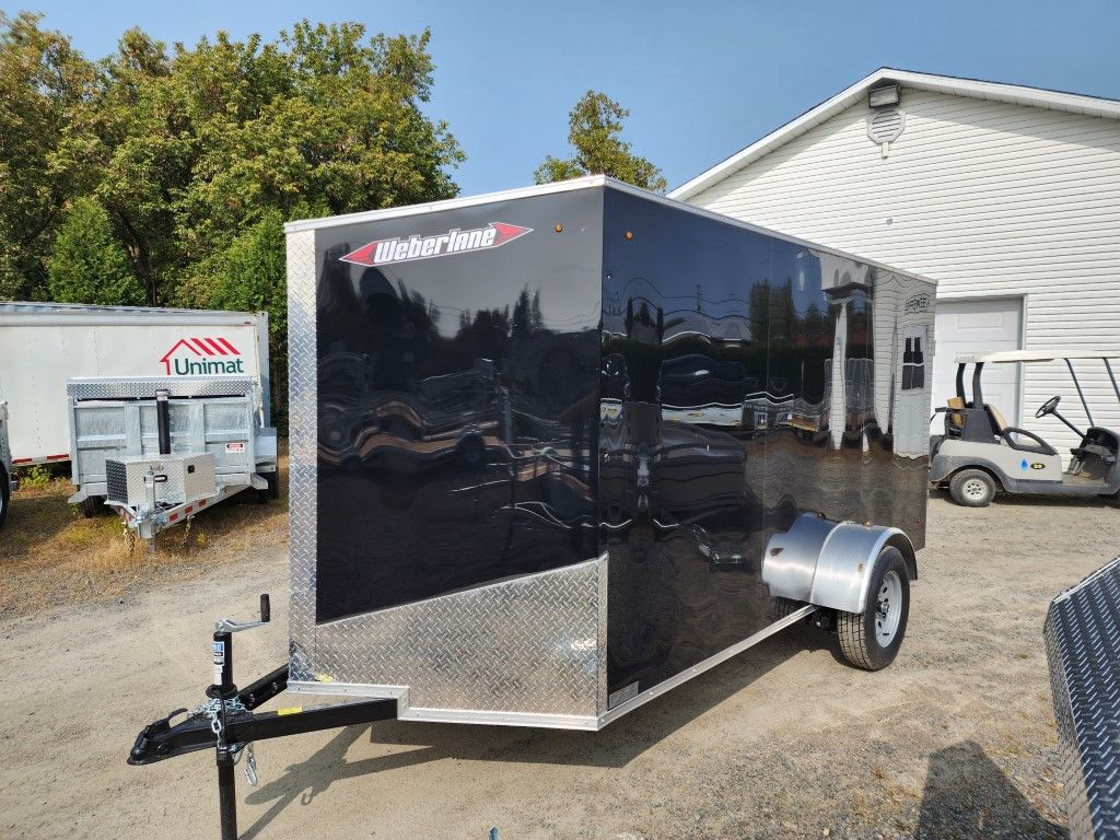 Remorque fermée noire et argentée dans un cadre extérieur ensoleillé.