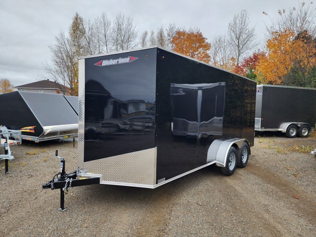 Remorque cargo noire fermée avec des accents argentés, stationnée à l'extérieur avec du feuillage d'automne en arrière-plan.