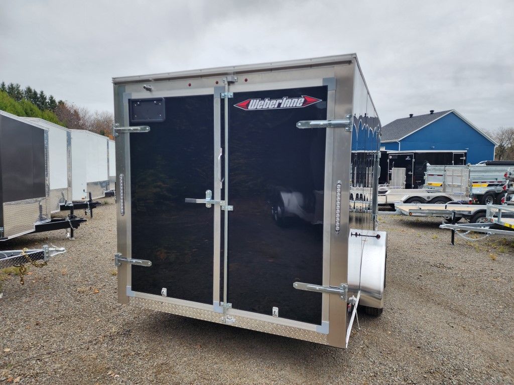 Remorque cargo noire fermée avec châssis et portes argentés, stationnée à l'extérieur sur du gravier.