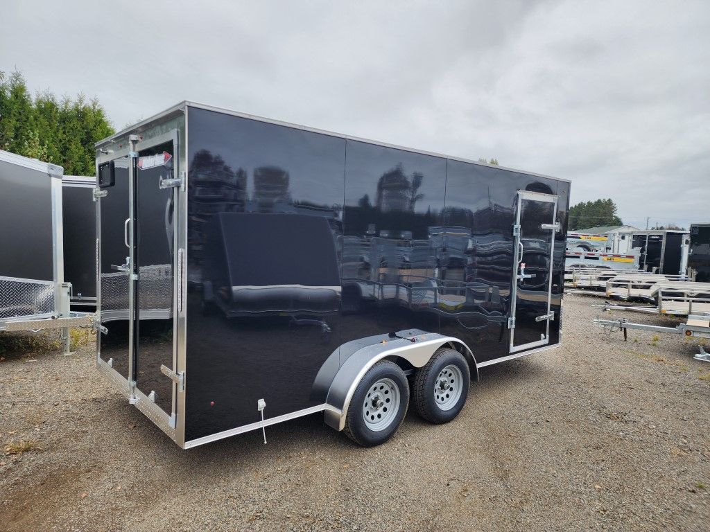 Remorque cargo noire fermée avec des accents argentés, stationnée sur un terrain en gravier.