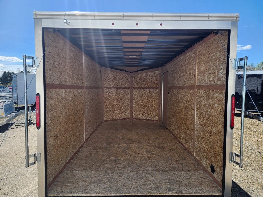 Intérieur de remorque de chargement vide avec murs OSB et portes ouvertes sous un ciel bleu.