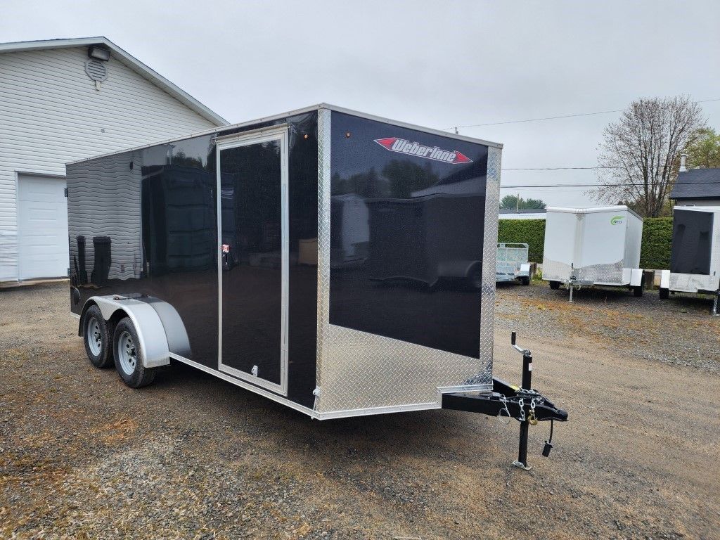 Remorque cargo fermée noire et argentée garée à l'extérieur par temps nuageux.