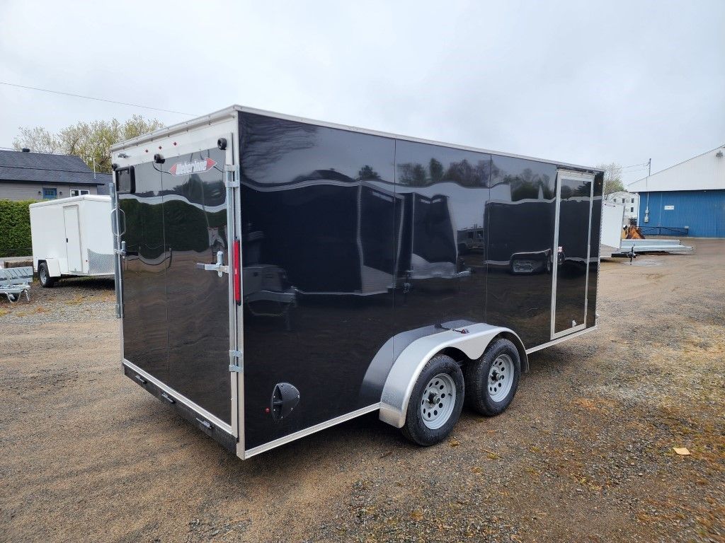 Remorque cargo fermée noire garée sur du gravier, avec roues jumelées et toit blanc.