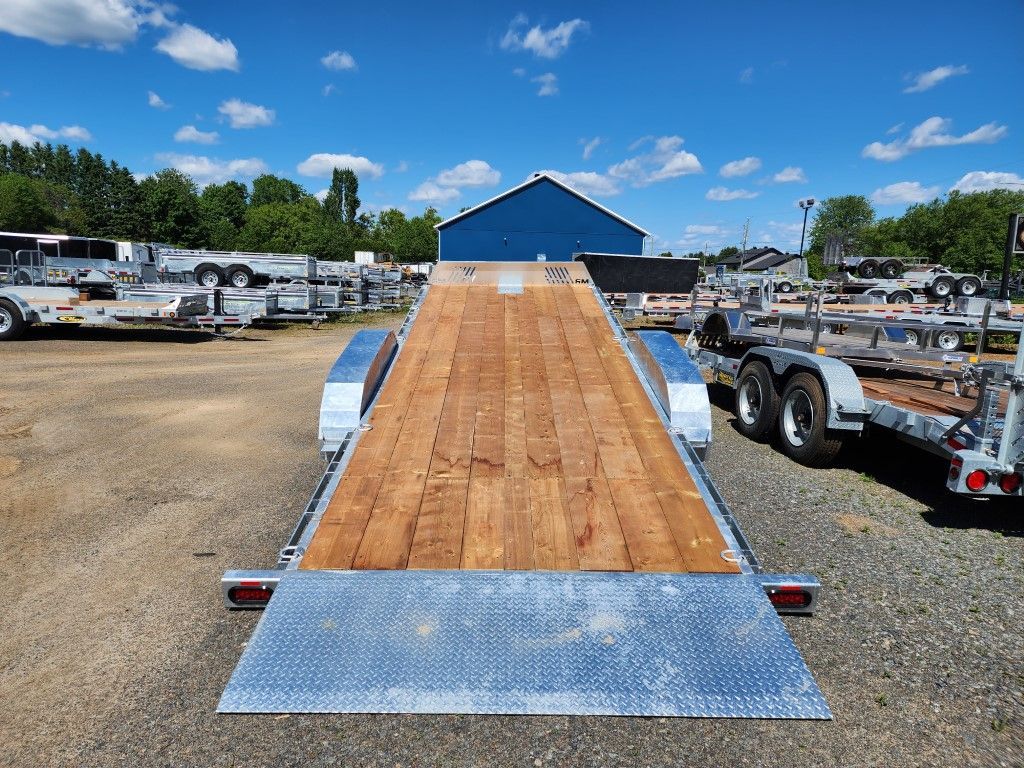 Une remorque à plateau avec un pont en bois et une rampe, à l'extérieur par une journée ensoleillée.