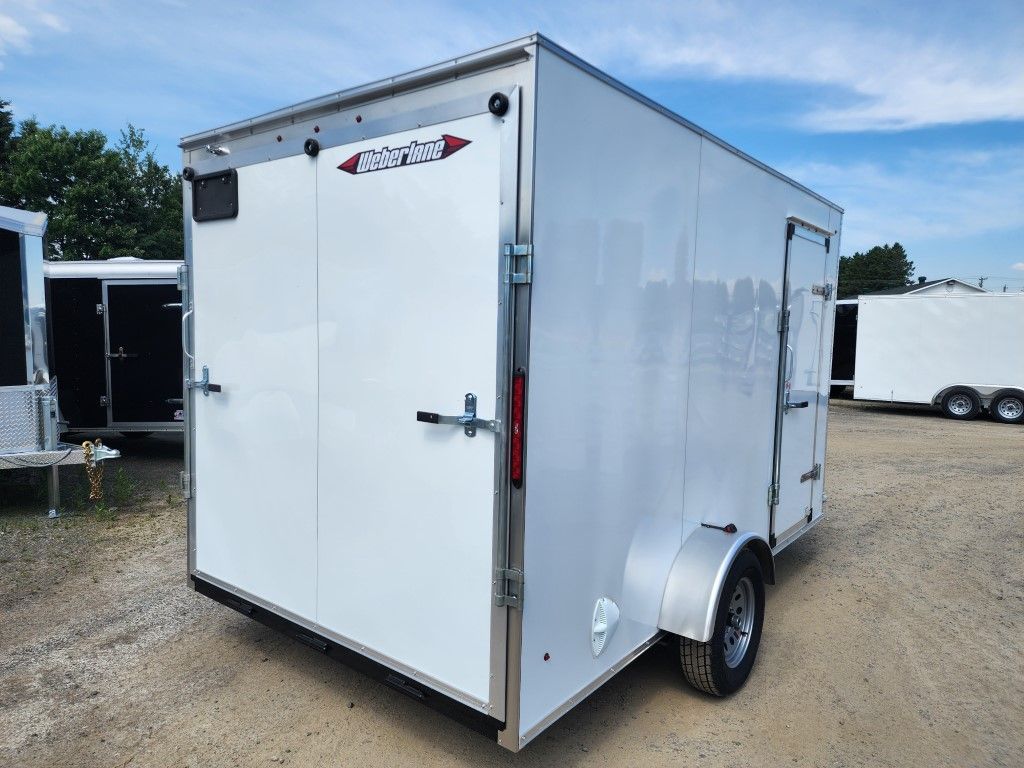 Remorque cargo fermée blanche sur terrain en gravier.