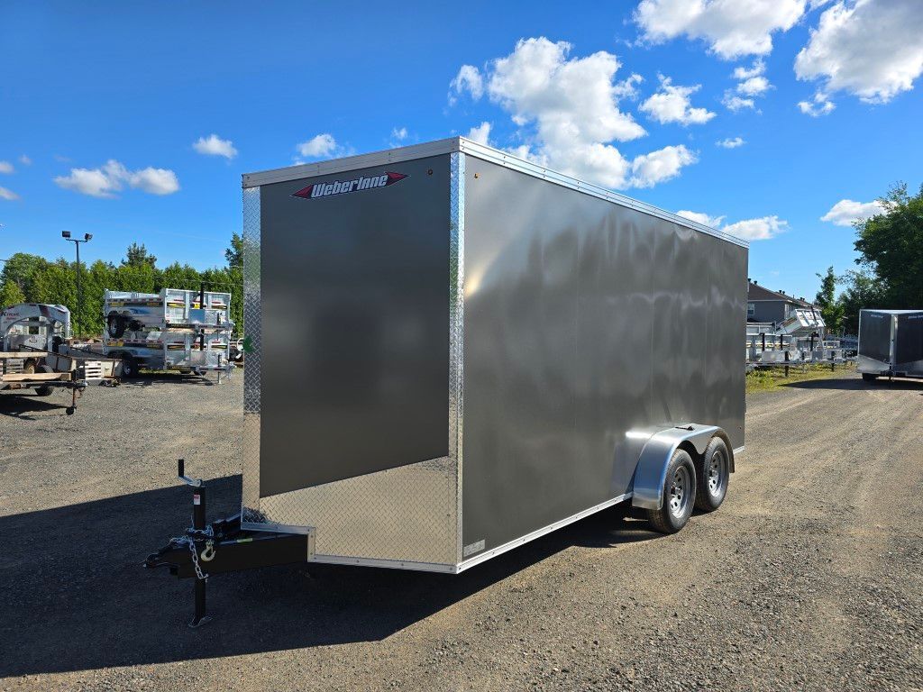 Remorque fermée argentée garée sur du gravier sous un ciel bleu vif.