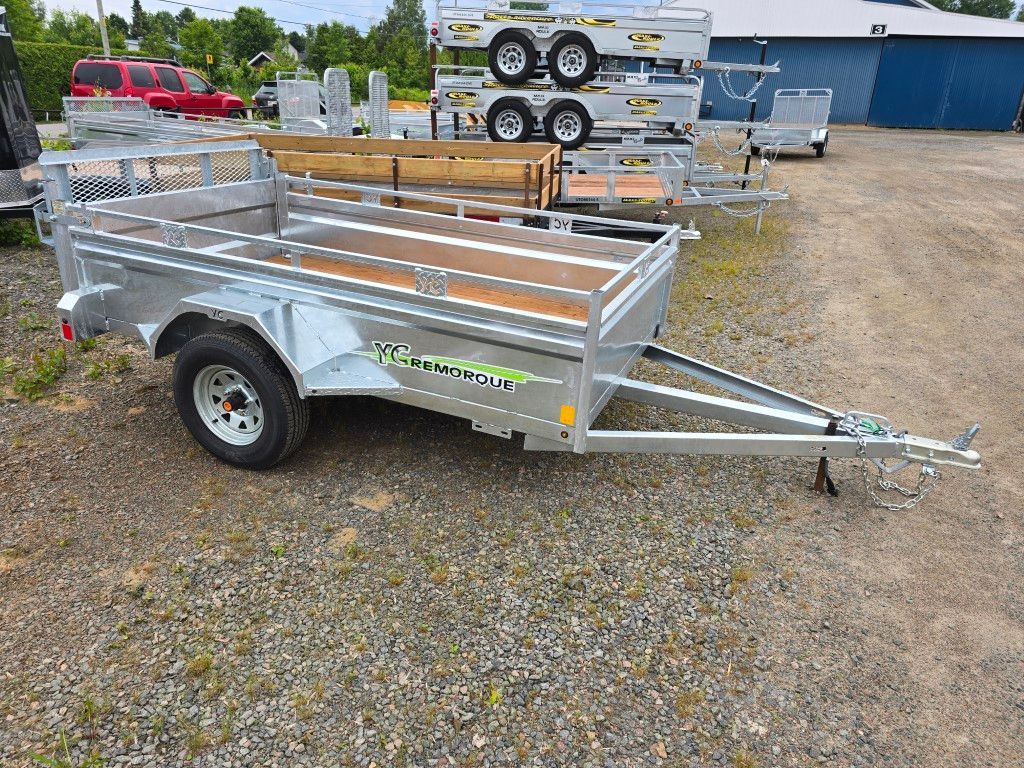 Une remorque avec une terrasse en bois est garée sur un terrain en gravier.