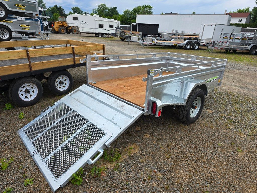 Une remorque avec une rampe est garée dans un terrain en gravier.