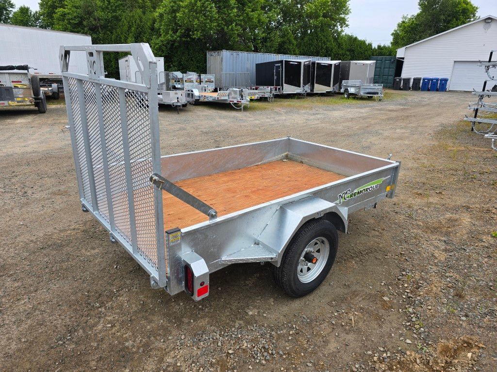 Remorque utilitaire argentée avec un arrière en filet dans un terrain en gravier.