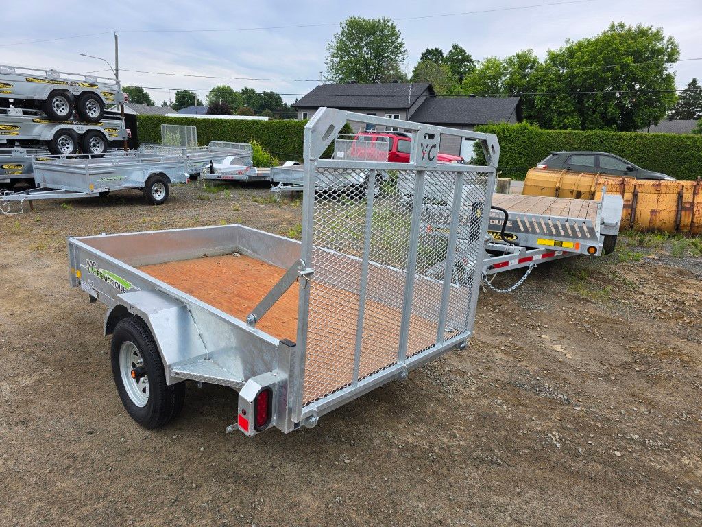 Remorque utilitaire argentée avec portail grillagé, garée à l'extérieur sur du gravier.