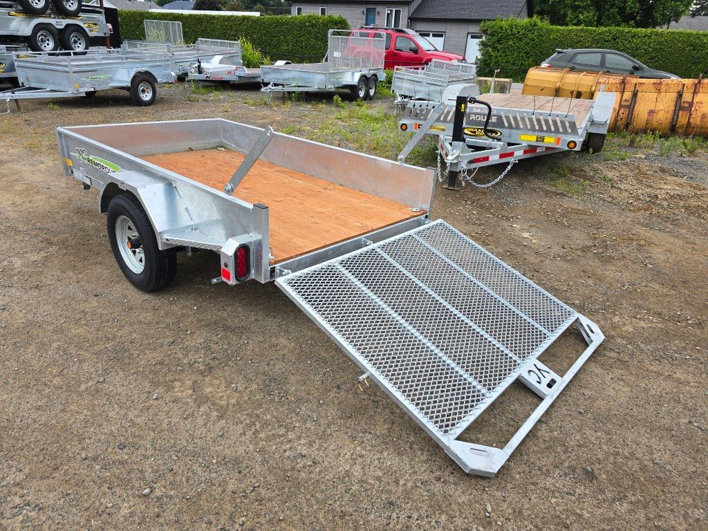 Remorque utilitaire argentée avec rampe ouverte, sol en gravier.