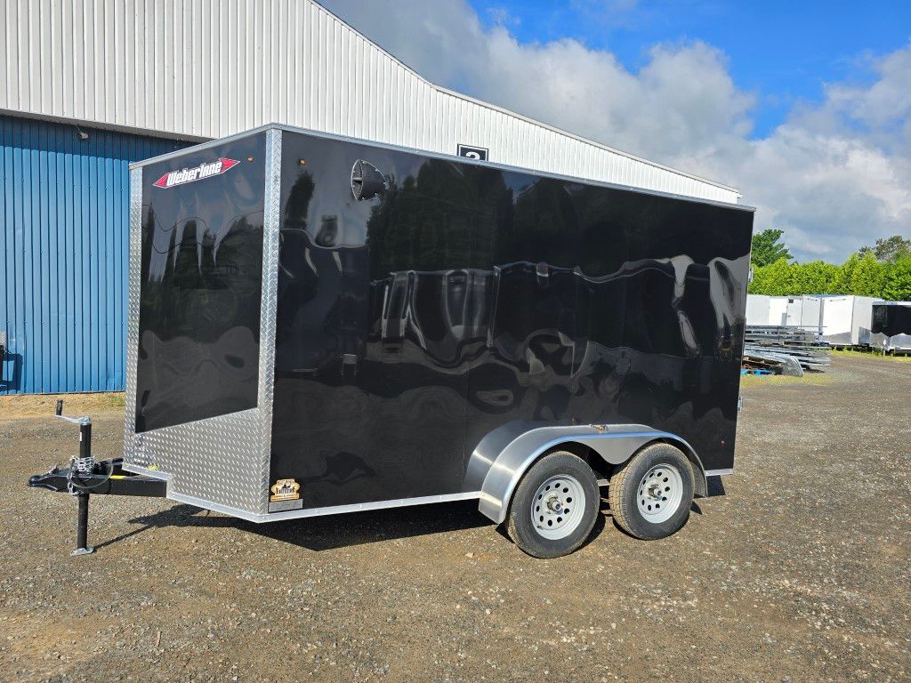 Une remorque noire est garée sur un terrain en terre devant un bâtiment.