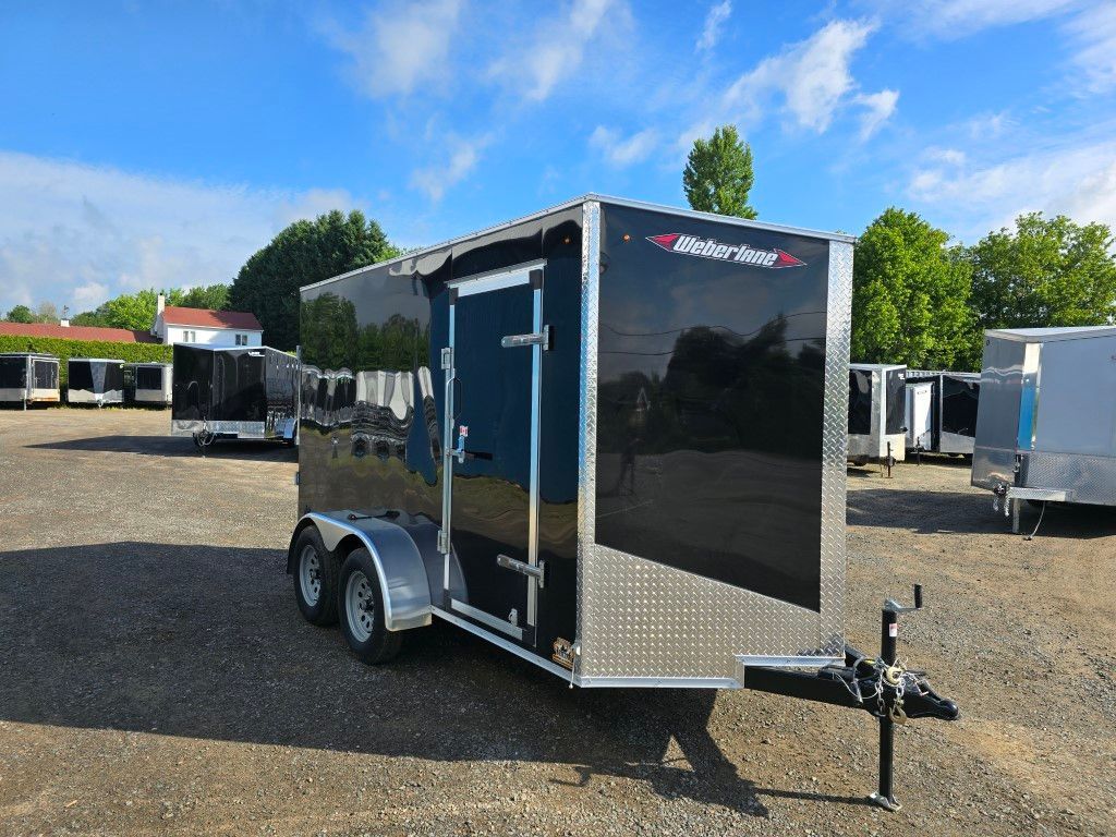 Remorque cargo fermée noire à deux roues, garée sur du gravier sous un ciel bleu.