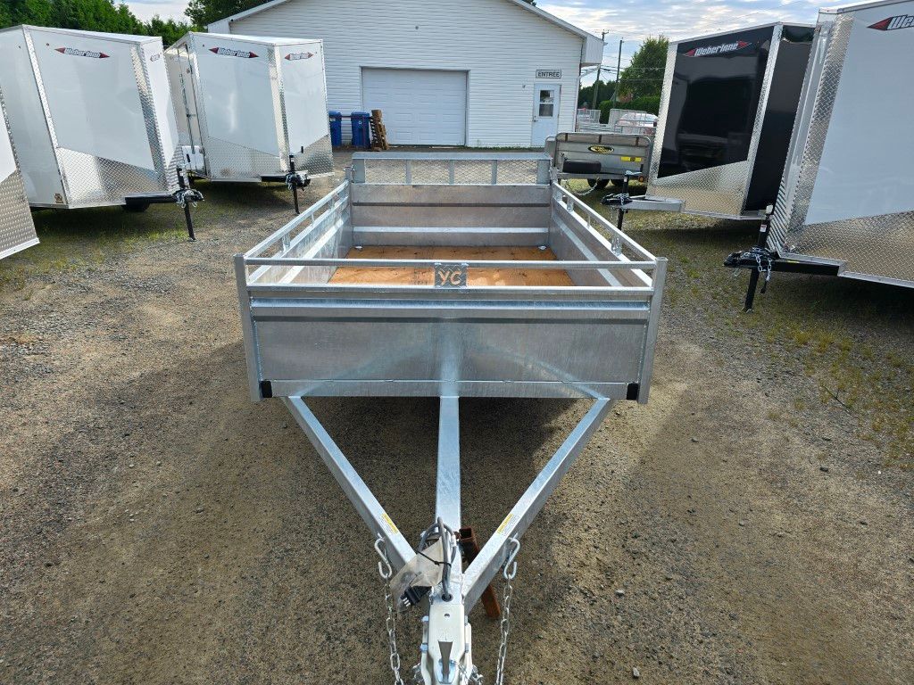 Remorque utilitaire ouverte en aluminium sur gravier, entourée d'autres remorques.