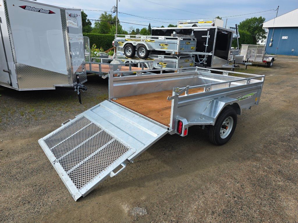 Remorque utilitaire argentée avec rampe de descente sur un terrain en gravier.