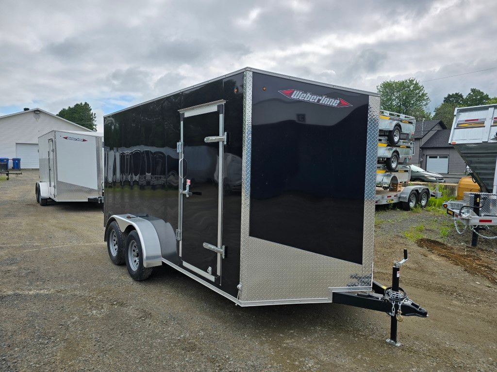 Une remorque noire et argentée est garée sur un terrain en terre.