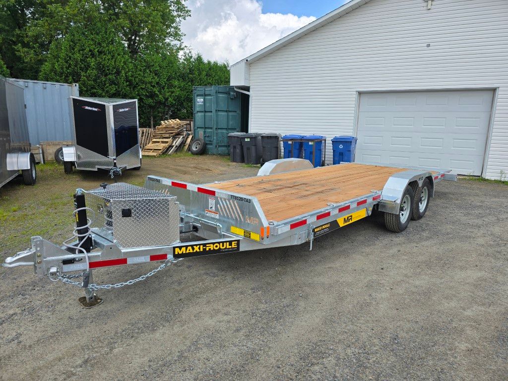 Une remorque à plateau est garée devant un garage.