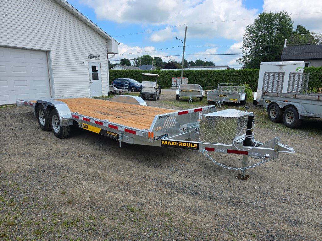 Une remorque à plateau est garée devant un garage.
