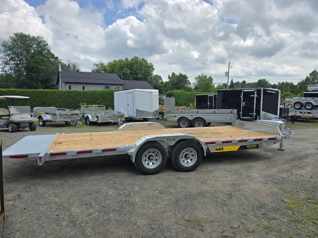 Une remorque à plateau est garée sur un terrain en gravier.