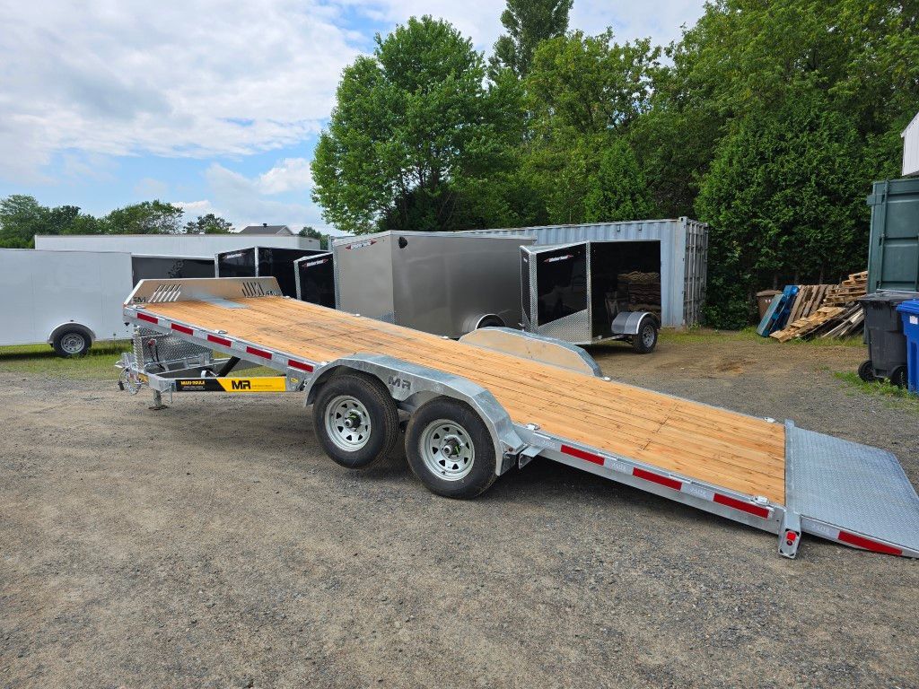 Une remorque à plateau est garée sur un terrain en gravier.