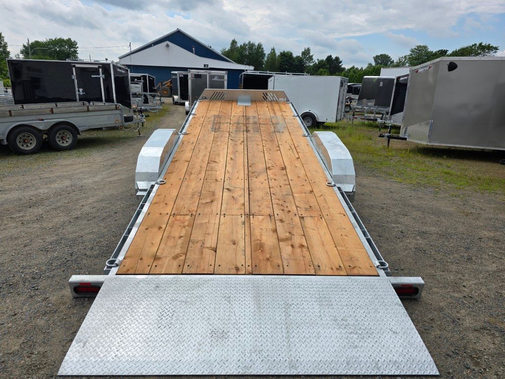 Une remorque à plateau est garée sur un terrain en gravier.