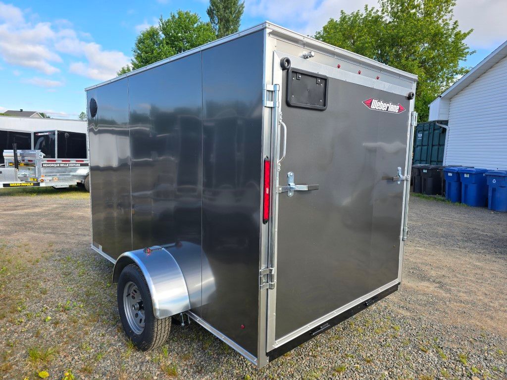 Une remorque noire est garée sur un terrain en gravier à côté d'une maison.