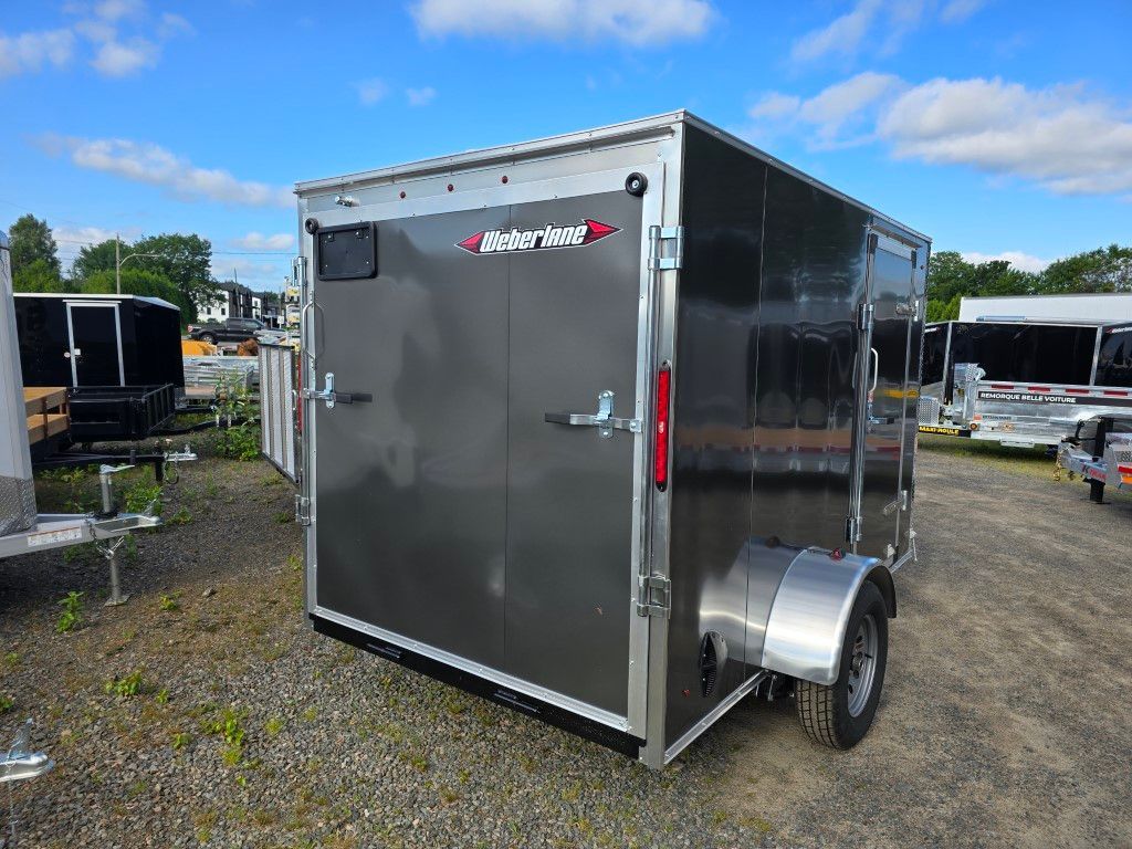 Une remorque grise est garée sur un terrain en gravier.