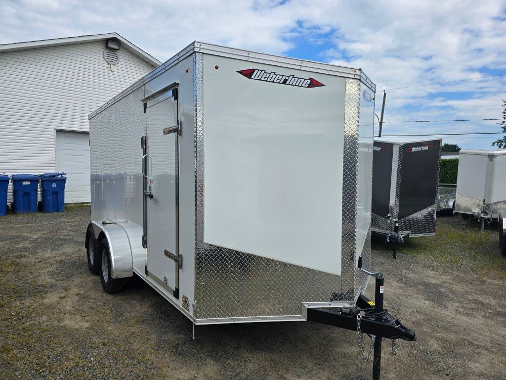 Une remorque blanche est garée sur un terrain en gravier devant un bâtiment.