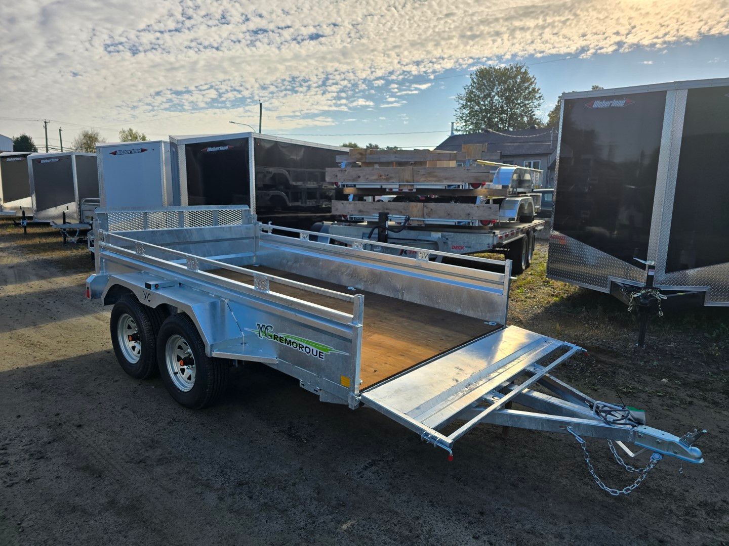 Remorque utilitaire argentée avec rampe, garée à l'extérieur sous un ciel nuageux.