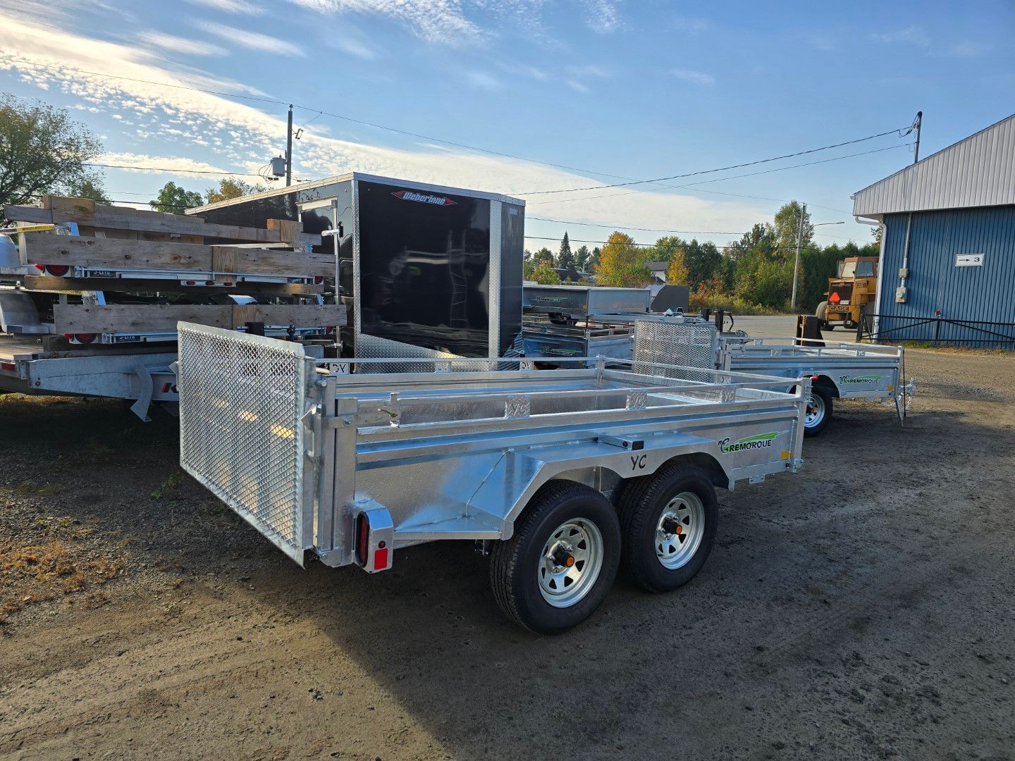 Remorque utilitaire en aluminium chargée de bois sur une surface de gravier sous un ciel bleu.