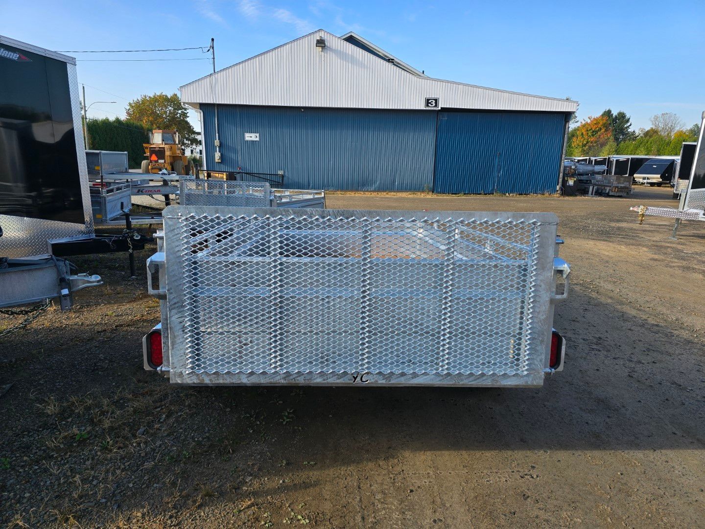 Remorque en métal avec côtés grillagés et un bâtiment en arrière-plan.