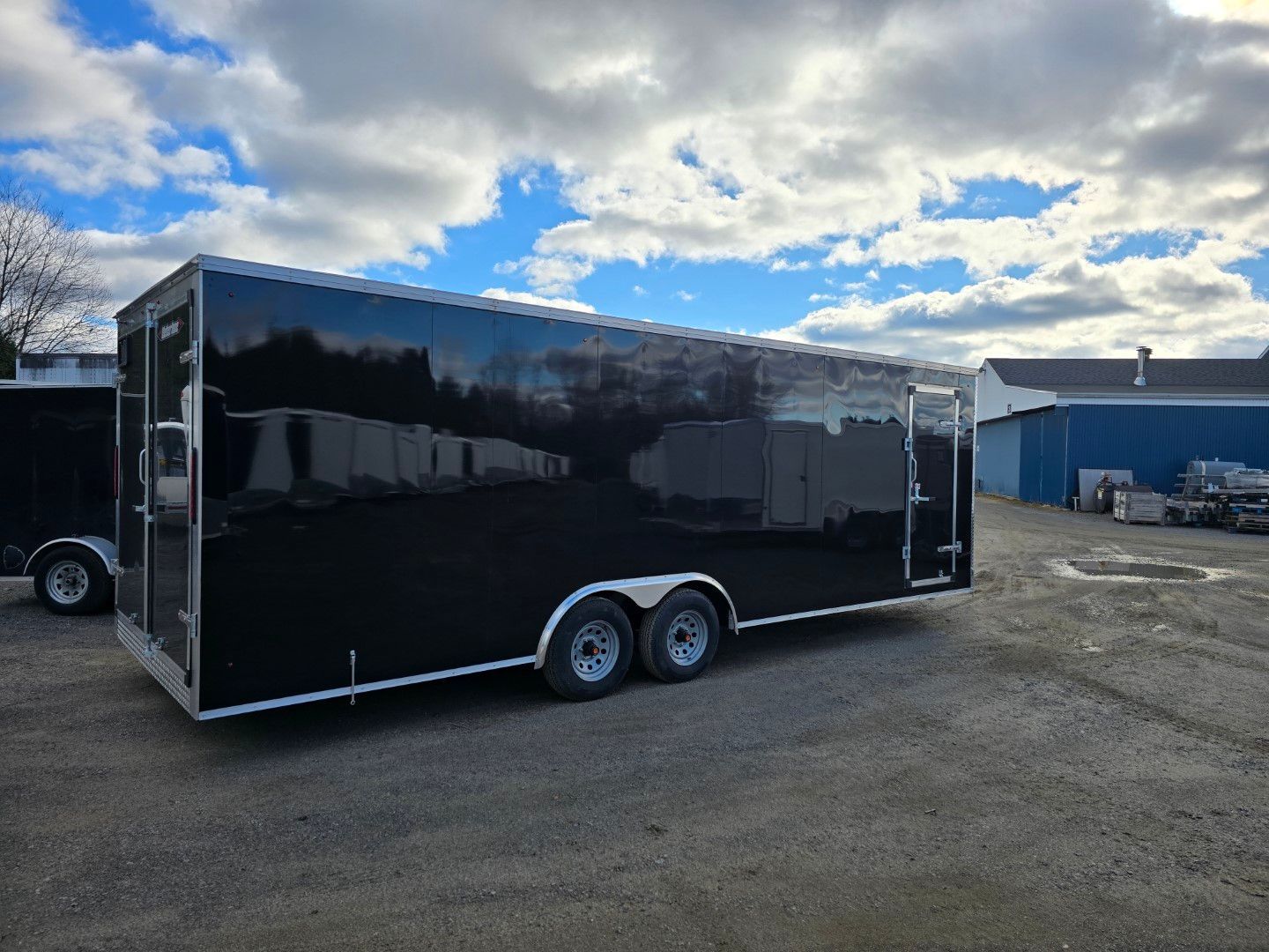 Une remorque noire est garée sur un parking devant un immeuble.