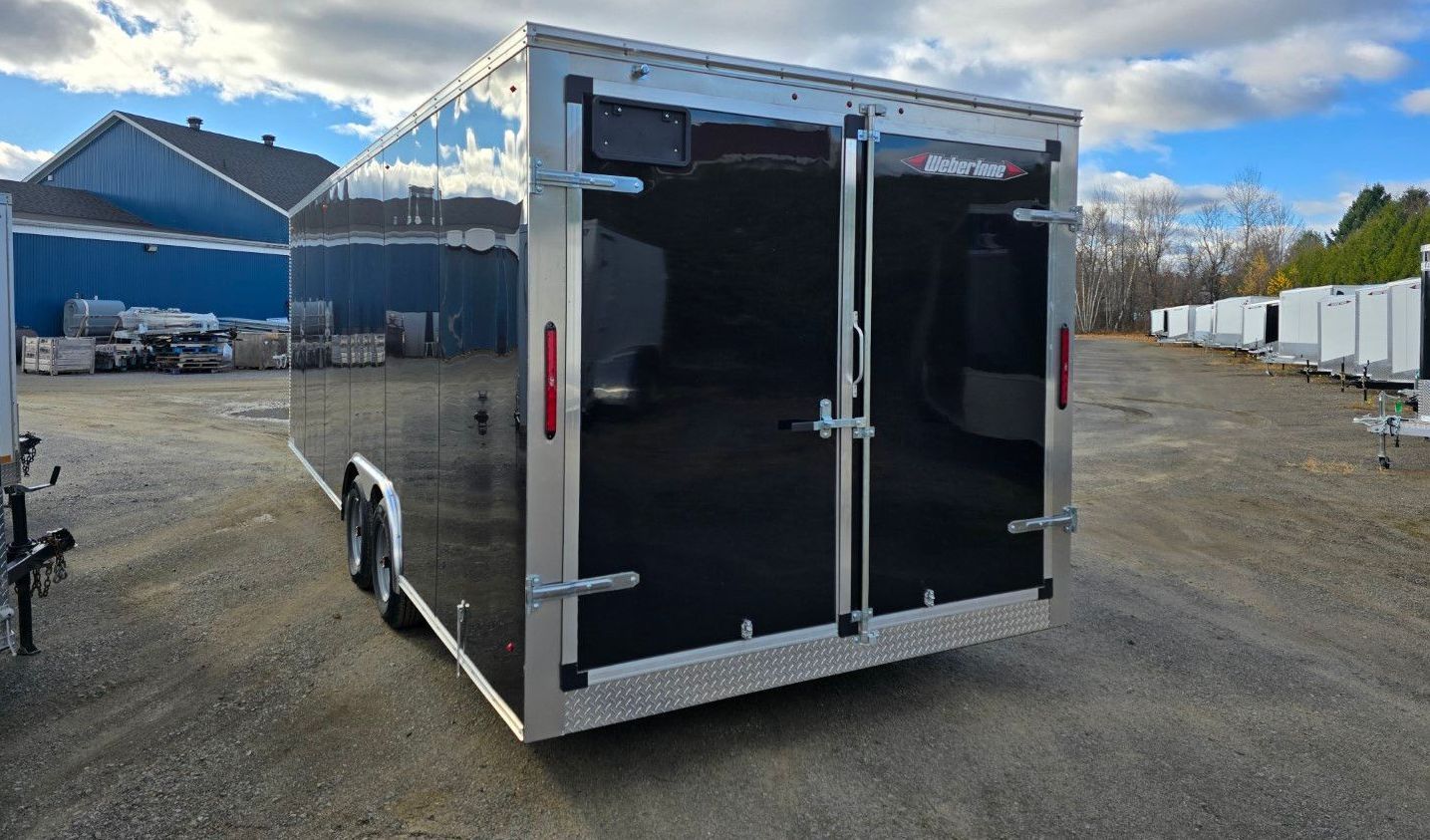 Une remorque noire et argentée est garée sur un terrain en gravier.