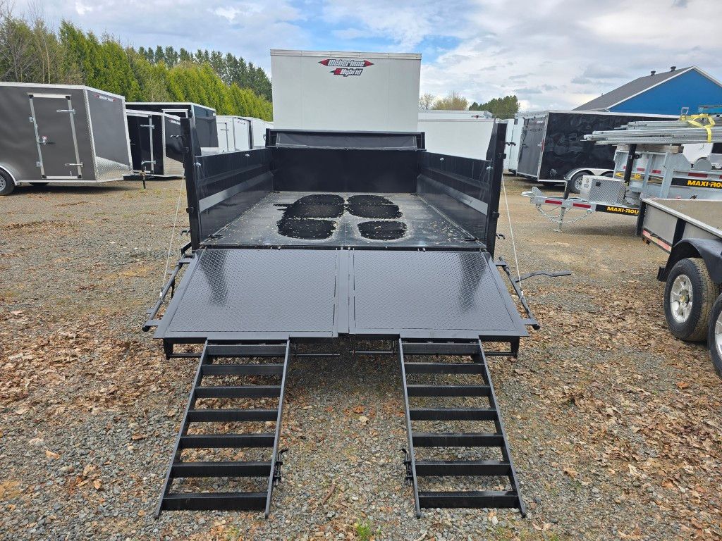Une remorque noire avec des rampes est garée sur un terrain en gravier.