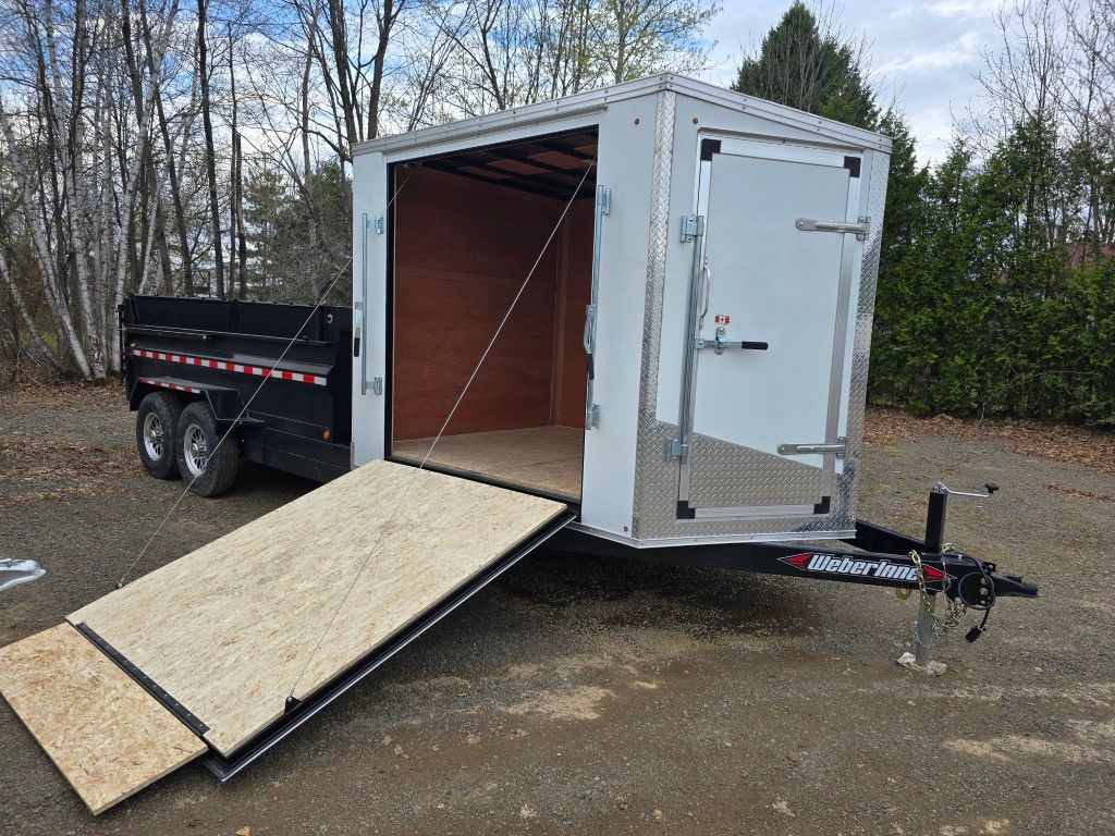 Une remorque avec une rampe attachée est garée dans un terrain en terre.