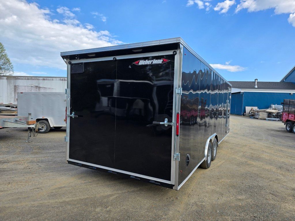 Une remorque noire est garée sur un terrain en terre devant un bâtiment.