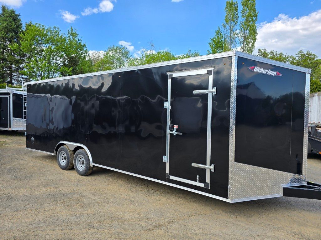 Une remorque noire est garée sur un terrain en terre.