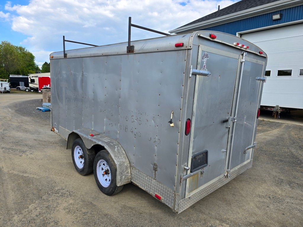 Une remorque argentée est garée sur un parking devant un immeuble.