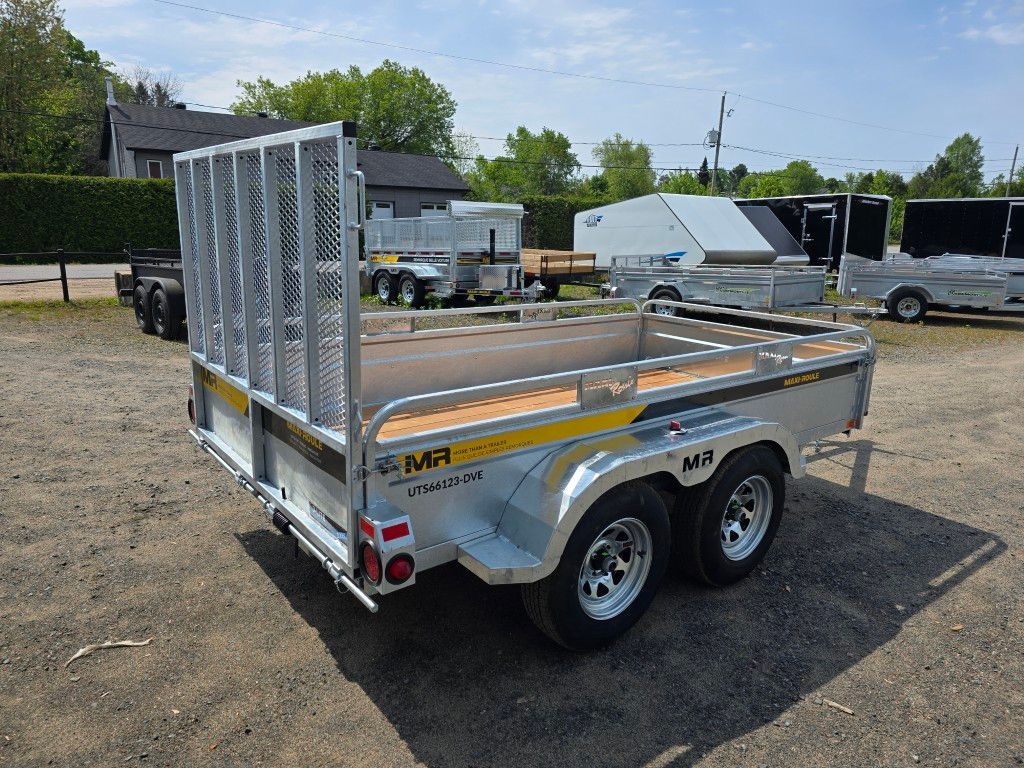 Une remorque avec une terrasse en bois est garée sur un terrain en terre.