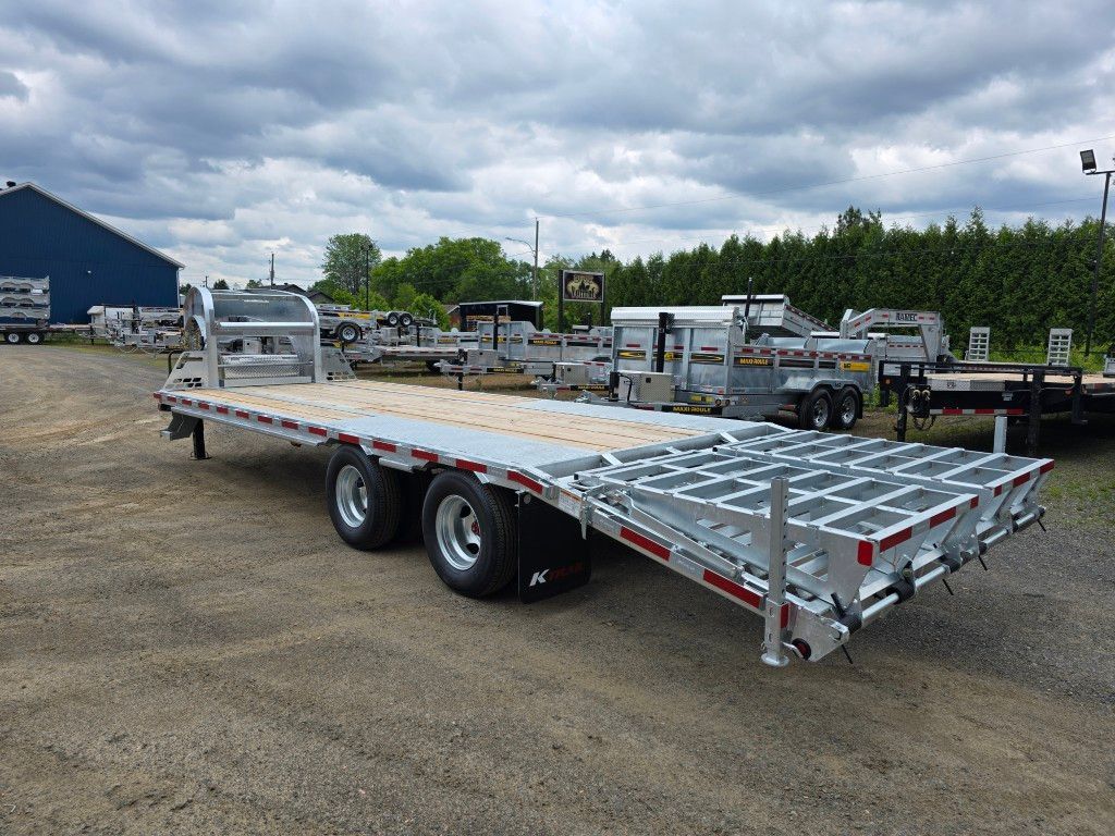 Une remorque à plateau est garée sur un terrain devant un bâtiment.