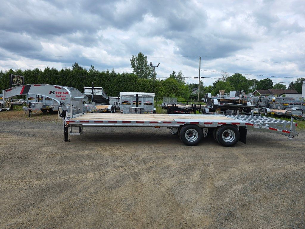 Une remorque à plateau est garée sur un terrain en gravier.