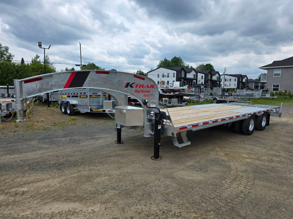 Une remorque à plateau est garée sur un terrain en gravier.