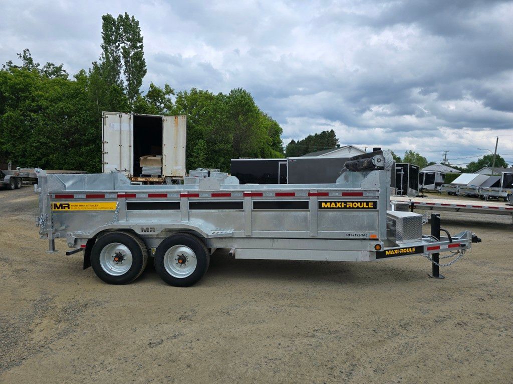 Remorque à benne argentée garée sur du gravier, sous un ciel nuageux.