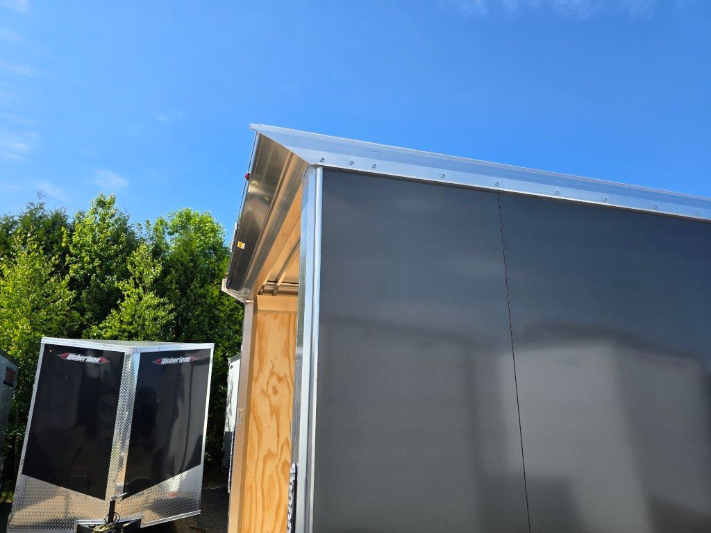 Remorque fermée noire avec garniture argentée contre un ciel bleu, des arbres en arrière-plan.