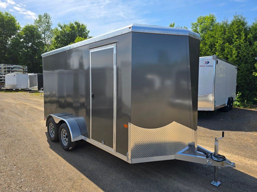 Remorque cargo fermée grise sur une surface de gravier avec deux autres remorques en arrière-plan.